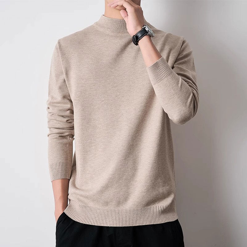 A man wearing a light beige knit mock-neck sweater, shown from the neck down against a plain light gray background.